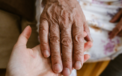 An older adult gently rests their hand in the open hand of a caregiver.